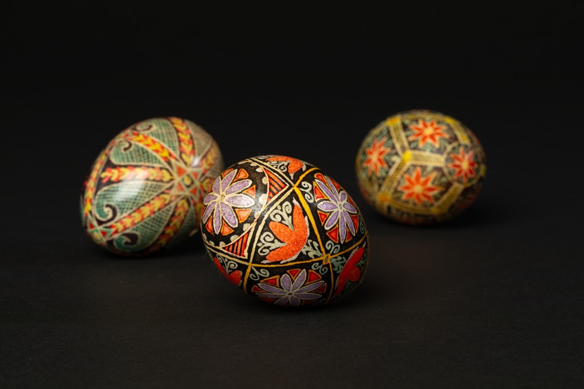 Tana Shane, Pysanky (Ukrainian Decorative Eggs), 20th Century. From Mingei International Museum's Permanent Collection.  

Image Description: Three intricately decorated eggs lying on a black background. The patterns on the egg are geometric and include symbols such as stars, flowers, and scrolls. The colors on the eggs include red, purple, yellow, green, and black.