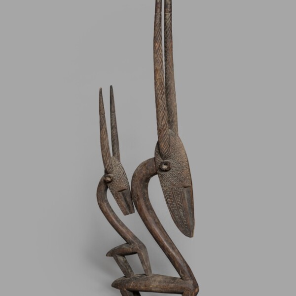 This wooden sculpture represents a chiwara—a mythological hero that is part human, part antelope. It was likely part of a headdress. There are two antelope sculptures with straight horns. One of the sculptures is smaller than the other.