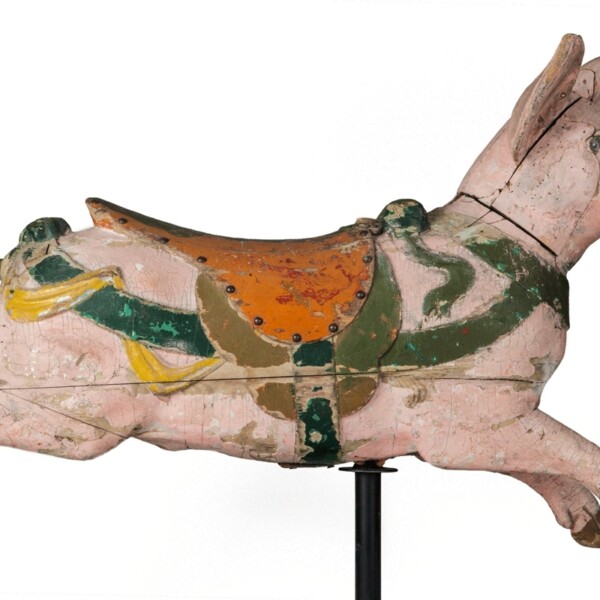 This carousel pig has a pink body with an orange and green saddle attached to its back. The stir-ups are green. It also has a green neck and body collar with yellow ribbon decorating the body collar. The black tail is curled and the pig is in a running form.