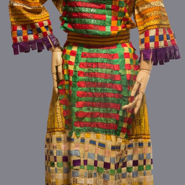 This dress is made of silk cigar bands and tobacco pouch labels. A package of ten or twenty cigars was held together by a colorful silk band advertising the tobacco brand. The bands and pouches vary in color, and most are yellow, purple, red, green, pink or blue.
