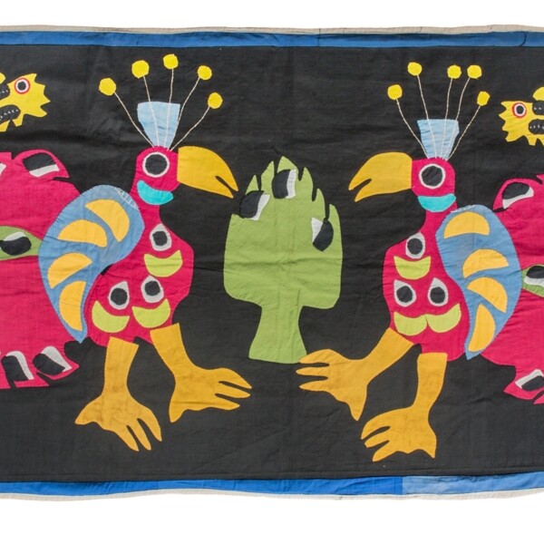 This textile is an appliquéd and sewn cotton banner typical of the Fon people of Benin. The textile is longer horizontally than vertically. The background is black and there are two large pink and blue stylized peacocks. The two peacocks cover the majority of the textile and are facing each other. In the upper right and left corner is one small yellow creature, possible a cat. In the center of the textile, in between the two peacocks is a large green motif, similar in shape to an artichoke.